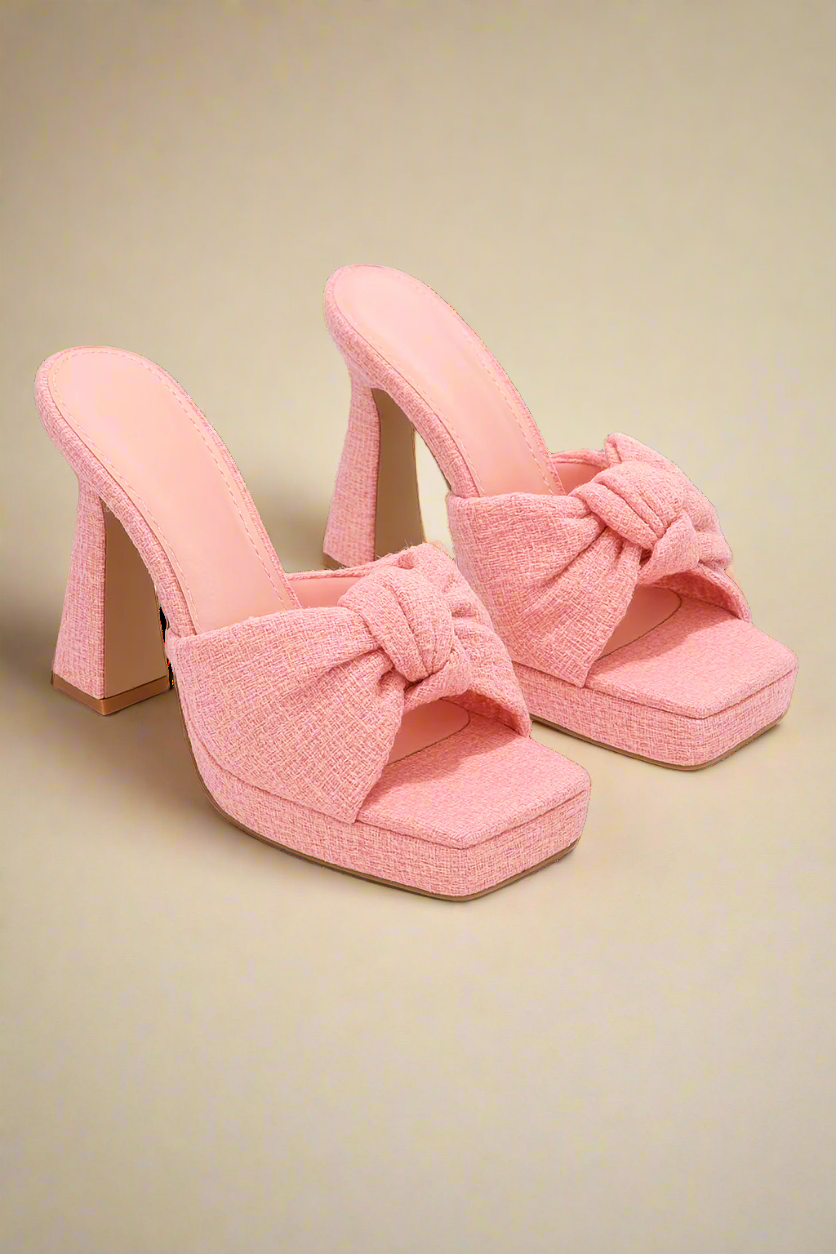 Pair of pink high-heeled shoes with bow details on a white background