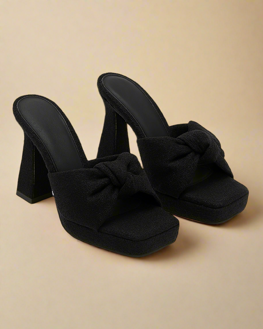 Black high-heeled sandals with bow details on a white background